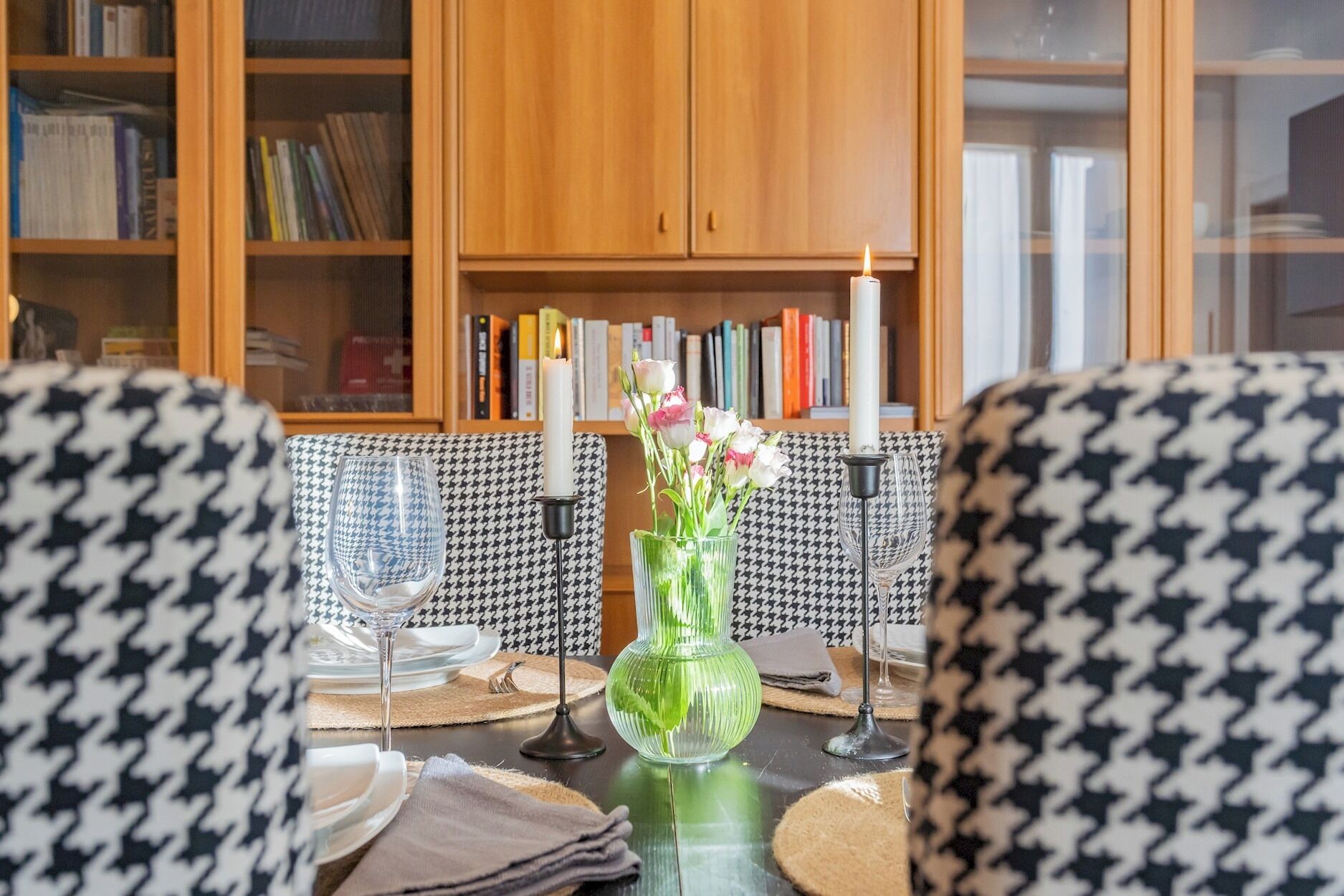 Un comedor con una mesa dispuesta para dos personas, un jarrón con flores y una vela encendida.