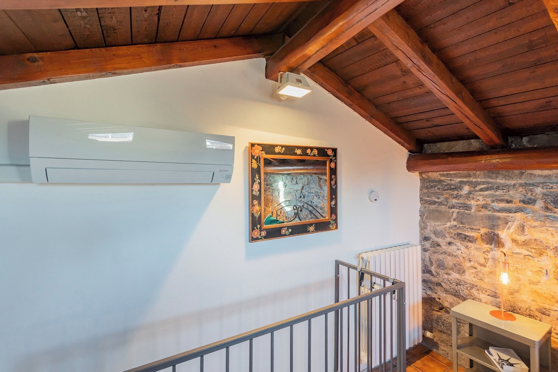 A staircase with a metal railing, a stone wall, and a small table with a lamp.