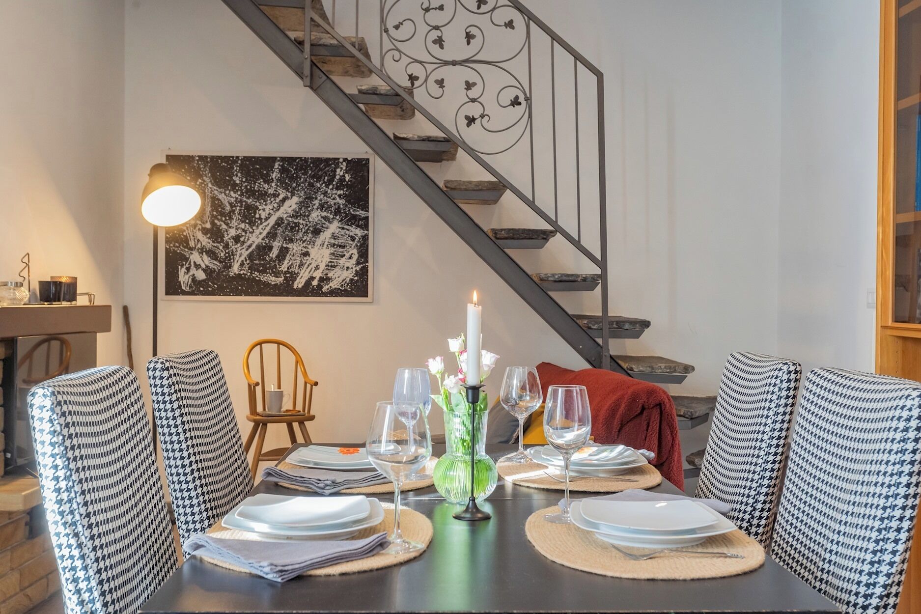 Zona pranzo con tavolo apparecchiato per quattro persone, una scala e un'opera d'arte incorniciata al muro.