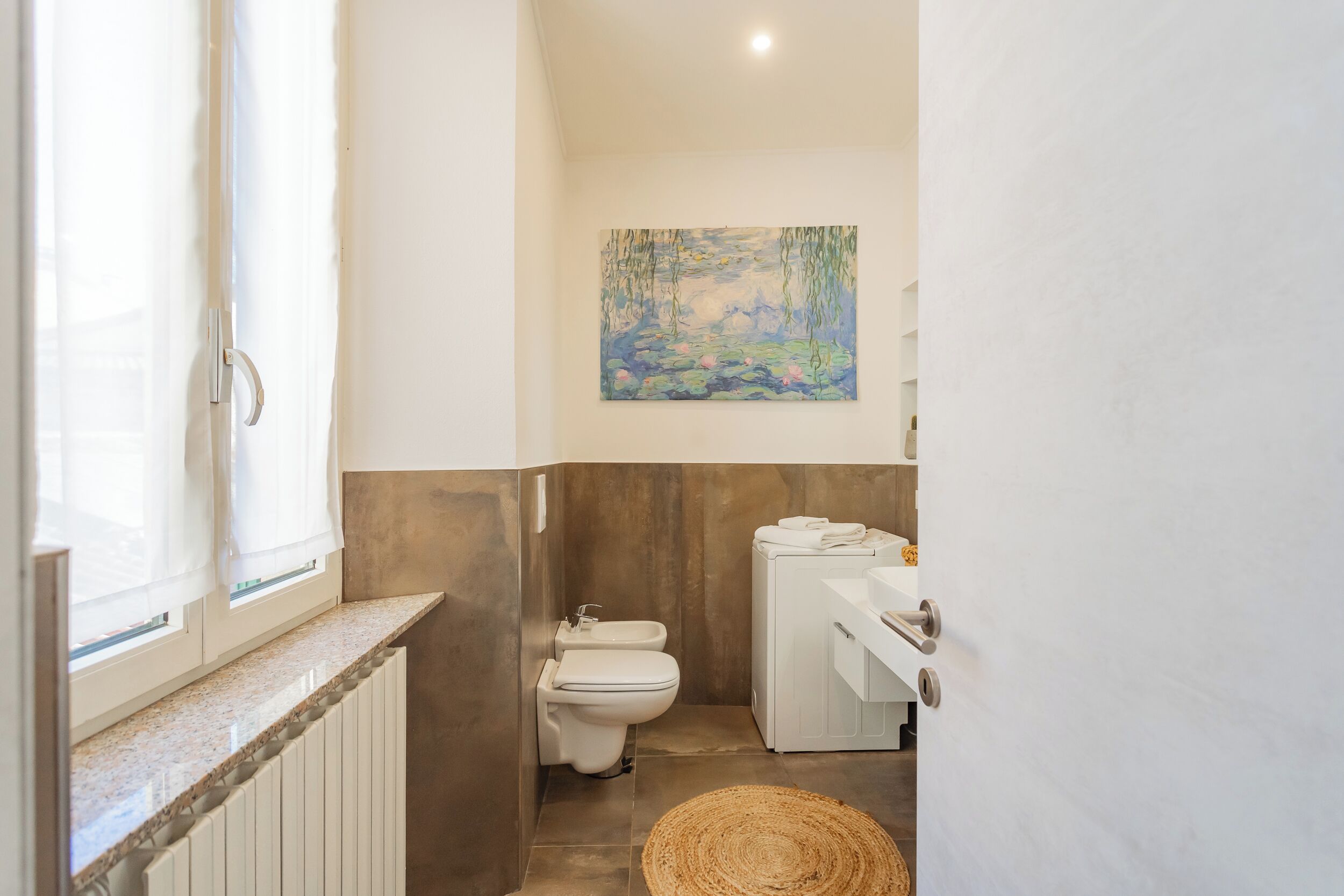 A bathroom with a toilet, sink, and a painting on the wall.