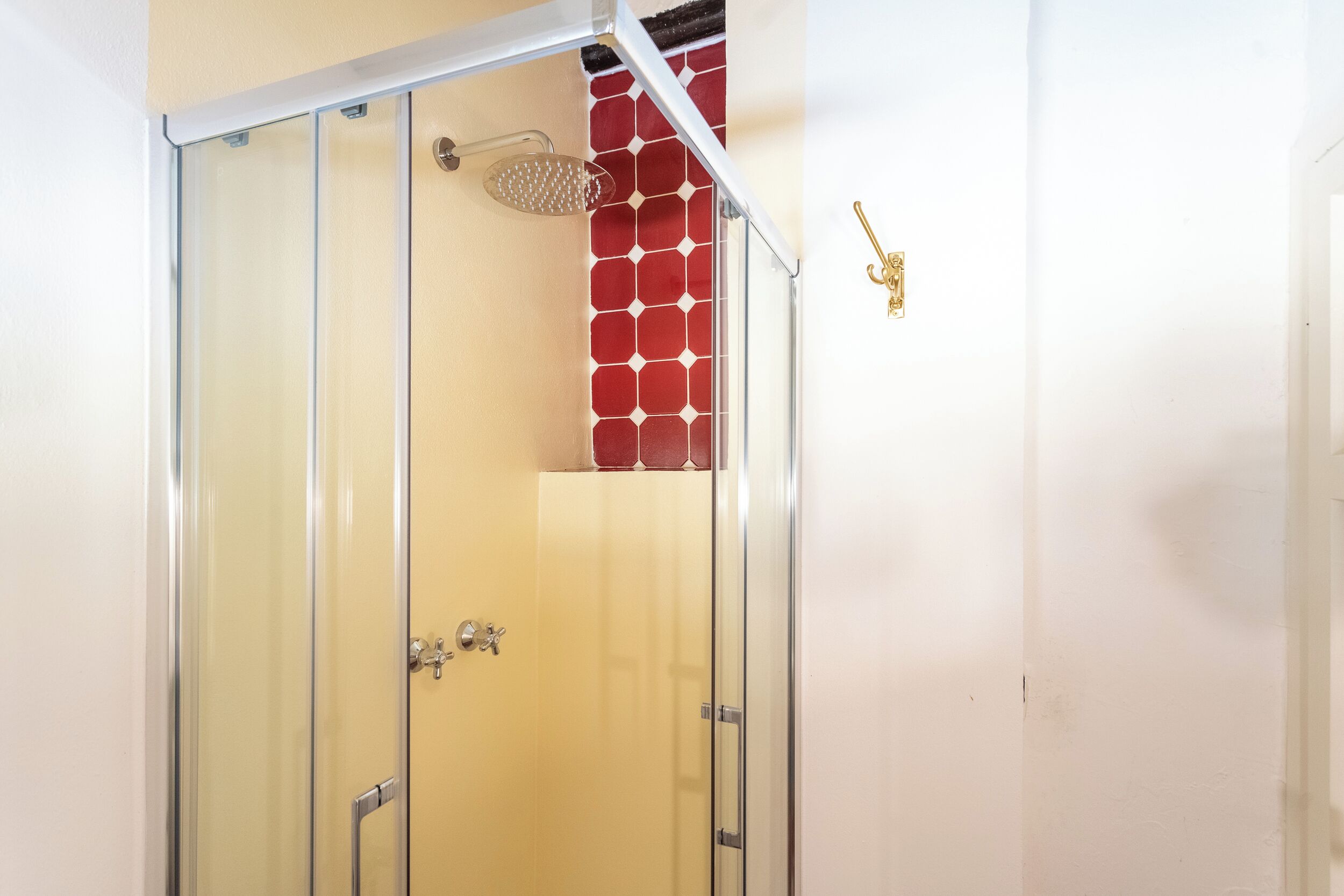 A glass-enclosed shower with a red-tiled wall and a gold keychain on the wall.