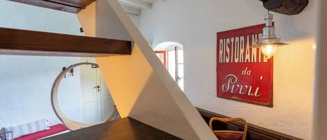 A dining area with a wooden table, a chair, a plate with food, a candle, and a wall sign reading "RISTORANZA da Pini".