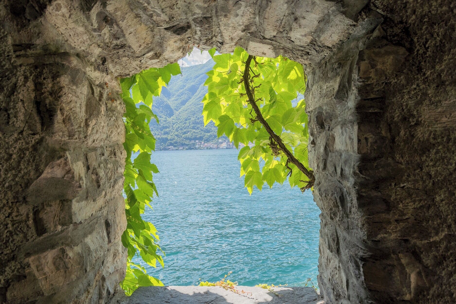 Une arche en pierre encadrant une vue sur un lac paisible et des montagnes lointaines.