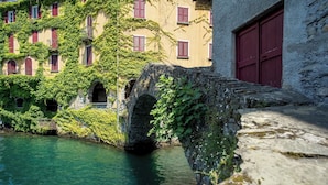A historic stone bridge over a canal, with ivy-covered buildings and a red door on the right.