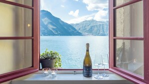 A bottle of champagne, two glasses, and a candle on a windowsill with a view of a lake and mountains.
