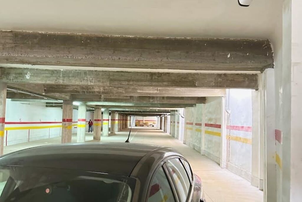Ett parkeringsgarage med betongpelare och en bil parkerad i förgrunden.