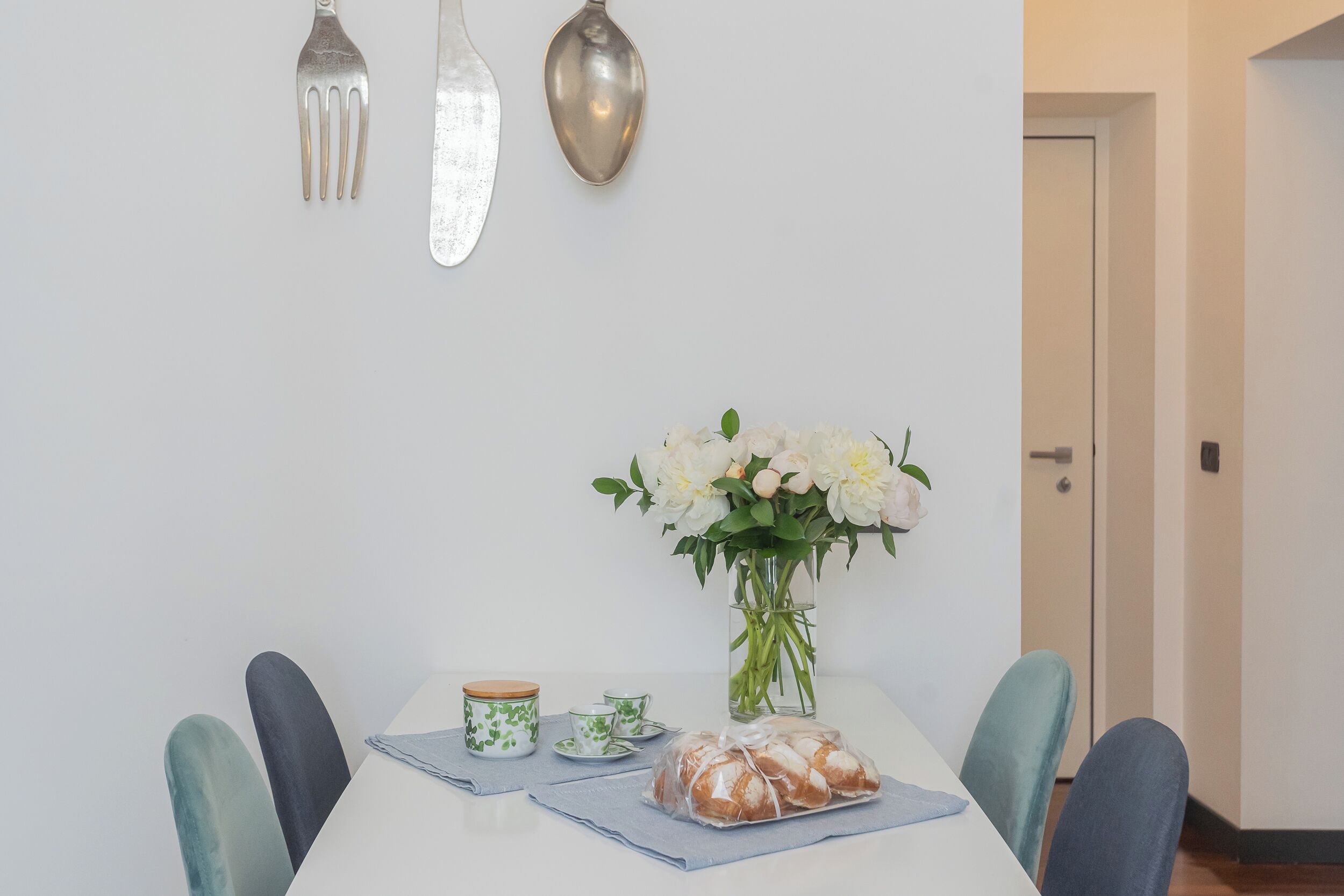 A dining table with a vase of white flowers, a loaf of bread, and matching tea sets.