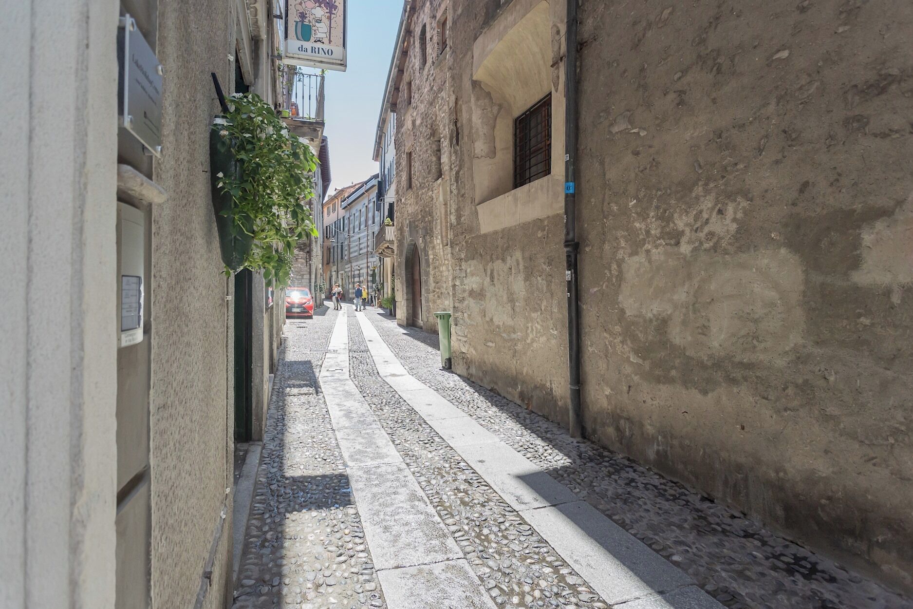 Una estrecha calle adoquinada bordeada por edificios antiguos con un letrero que dice "da RINO".