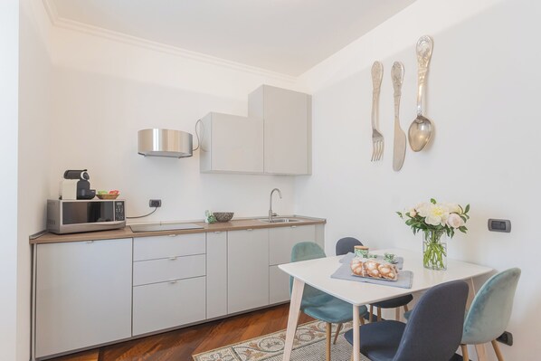 A compact kitchen with a microwave, toaster, and sink. There is a dining table with chairs and a vase of flowers.