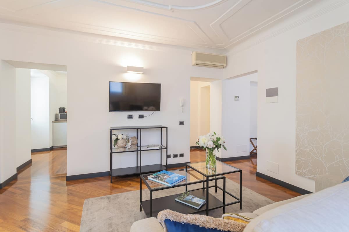 Una sala de estar moderna con una televisión de pantalla plana, una cafetera, una estantería y una mesa de centro con una revista.