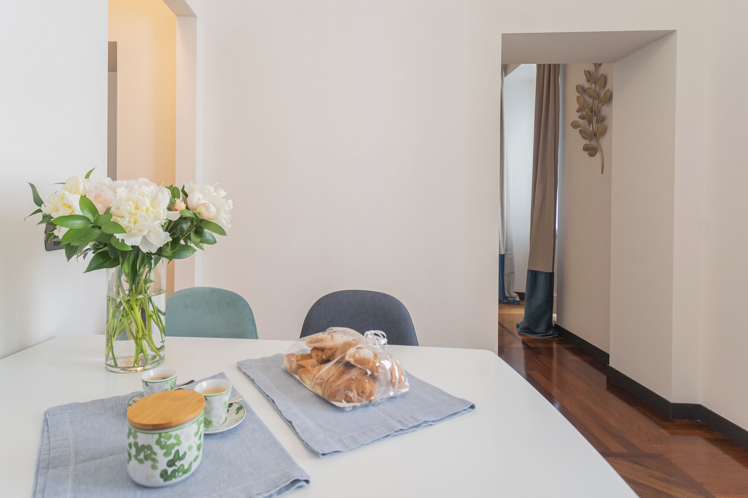 Una mesa de comedor con un florero de flores, una bolsa de pan y una taza de café.