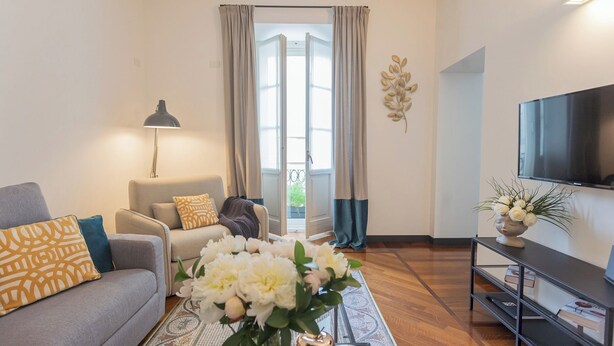 Un salon avec un canapé, une table basse ornée de fleurs, une lampe, un téléviseur et une bibliothèque.