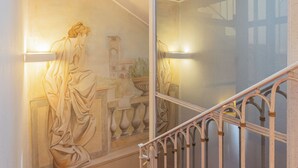 Un escalier orné d’une rampe en fer forgé et d’une fresque murale représentant une scène classique.