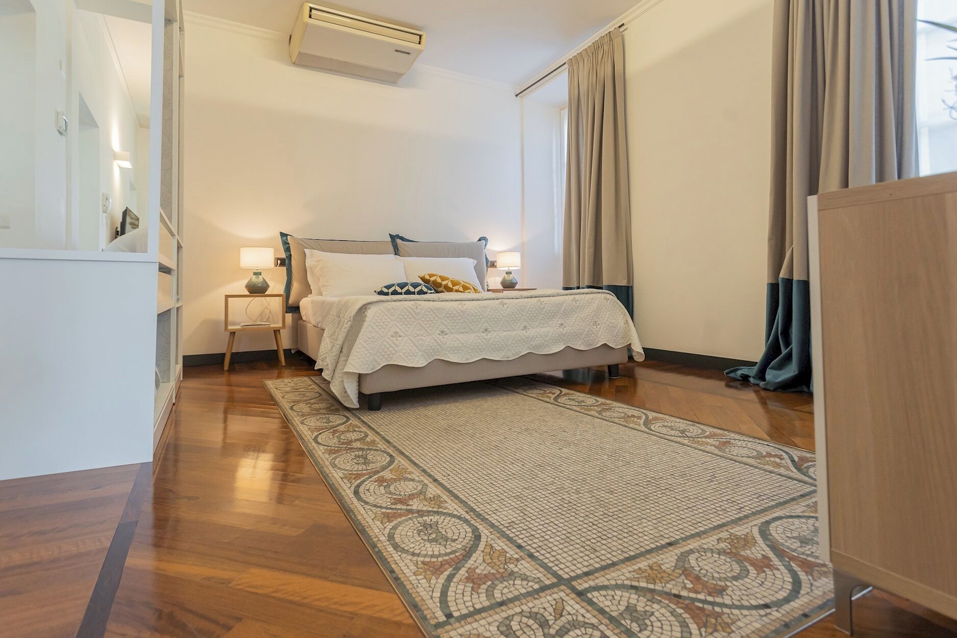 A bedroom with a bed, bedside lamps, a rug, and a wardrobe.