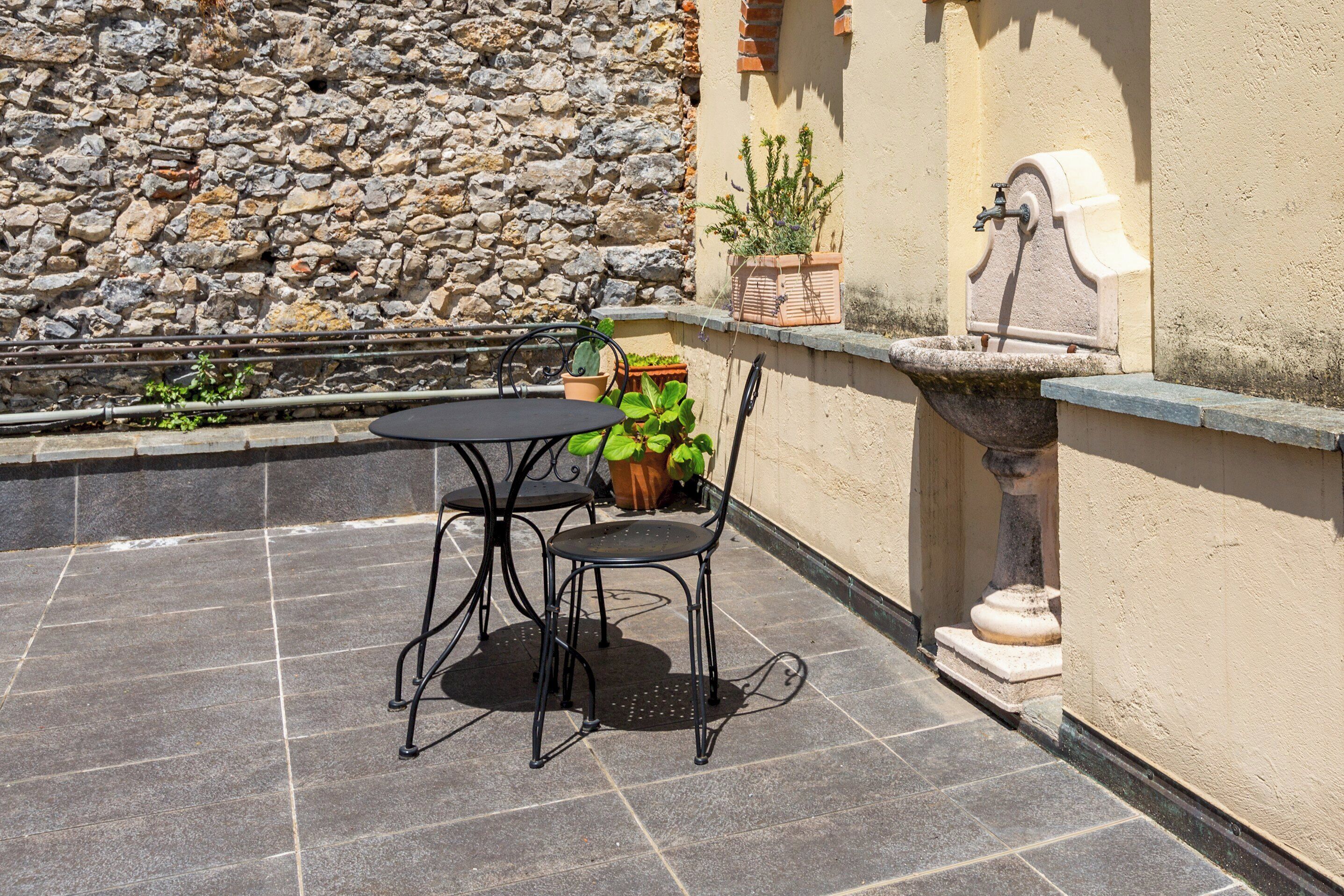 Un patio al aire libre con un muro de piedra, una mesita con dos sillas y una fuente de agua.