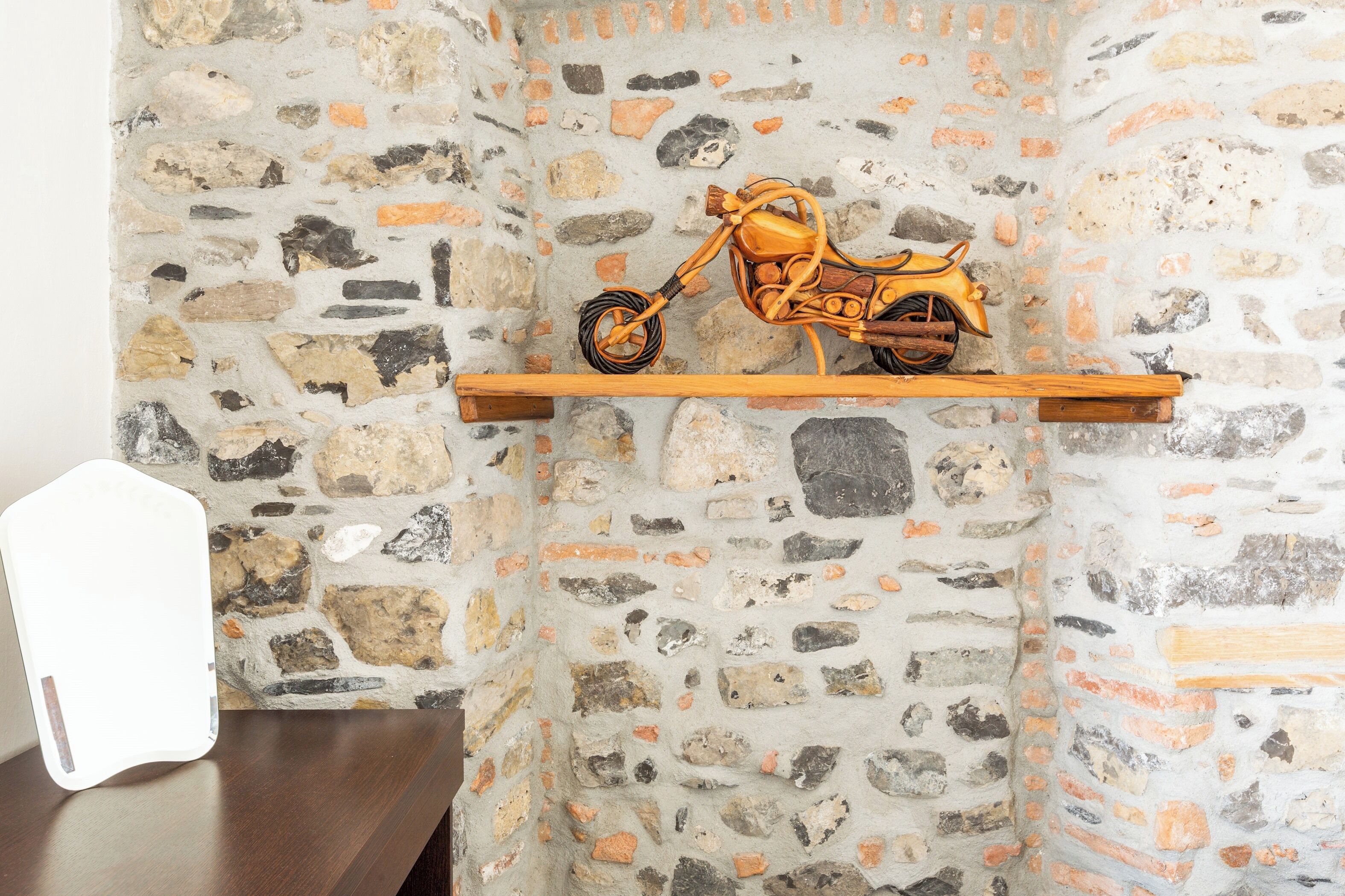 Un mur de pierre sur lequel est fixée une étagère en bois, et sur laquelle est posée une maquette de moto.