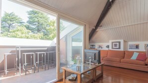 Un vaste espace de vie avec une porte-fenêtre coulissante donnant sur une terrasse extérieure, une table basse en bois, un canapé et un téléviseur.