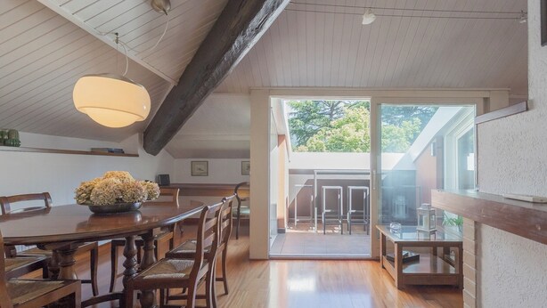 Un coin repas avec une table et des chaises en bois, un luminaire suspendu et une vue sur l’extérieur grâce à une porte vitrée.
