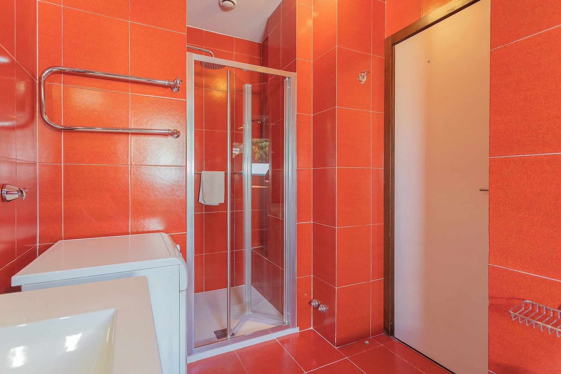 Ein Badezimmer mit roten Fliesen, einer Duschkabine aus Glas und einem weißen Waschbecken.
