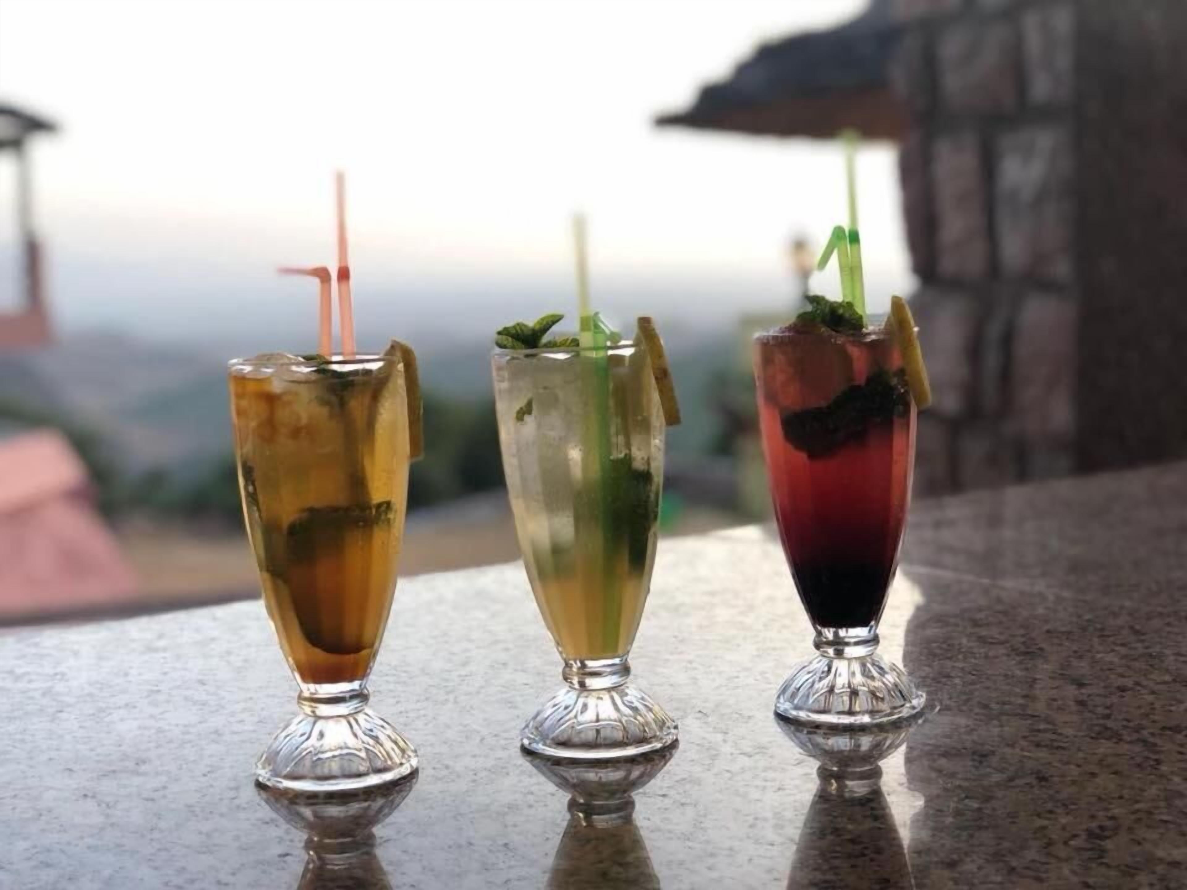 Tres bebidas sobre una barra con vista a un paisaje urbano de fondo.