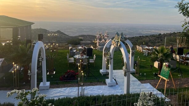 An outdoor wedding setup with a view of the sea, featuring white arches, tables, and chairs arranged on a grassy area. - Maison D'hôtes Yamine (Beni Mellal)