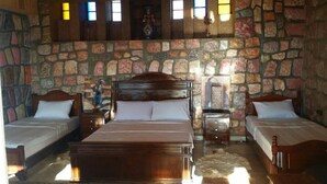 A room with a stone wall, two single beds, a large bed, and a wooden headboard. - Maison D'hôtes Yamine (Beni Mellal)