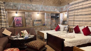 A cozy room with a stone fireplace, a bed with red and white bedding, a wooden coffee table, and a patterned rug. - Maison D'hôtes Yamine (Beni Mellal)