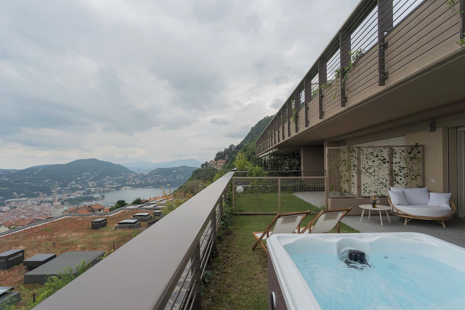 Un espacio exterior moderno con jacuzzi, sillones de descanso y vistas a un lago y montañas.