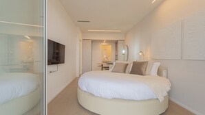 Un dormitorio moderno con una cama redonda, un televisor montado en la pared y una mesita de noche con lámpara.