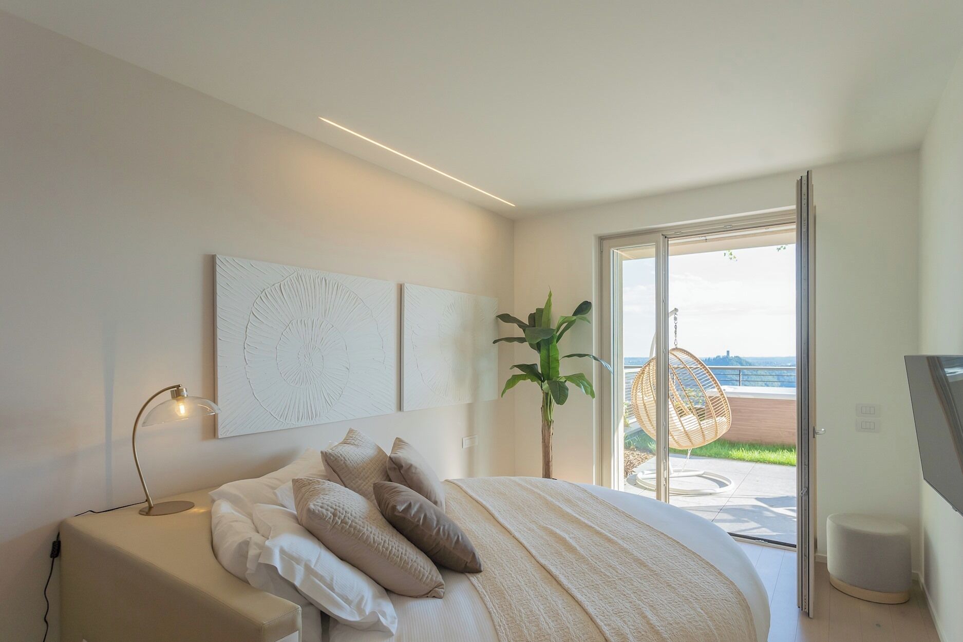 Ein modernes Schlafzimmer mit einem großen Bett, einer Pflanze und Blick ins Freie.