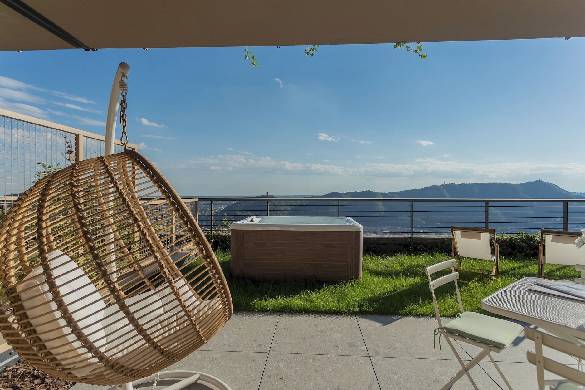 A patio with a hanging chair, a hot tub, and a table with chairs.