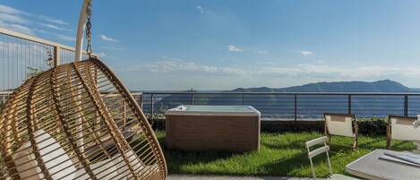 A patio with a hanging chair, a hot tub, and a table with chairs.