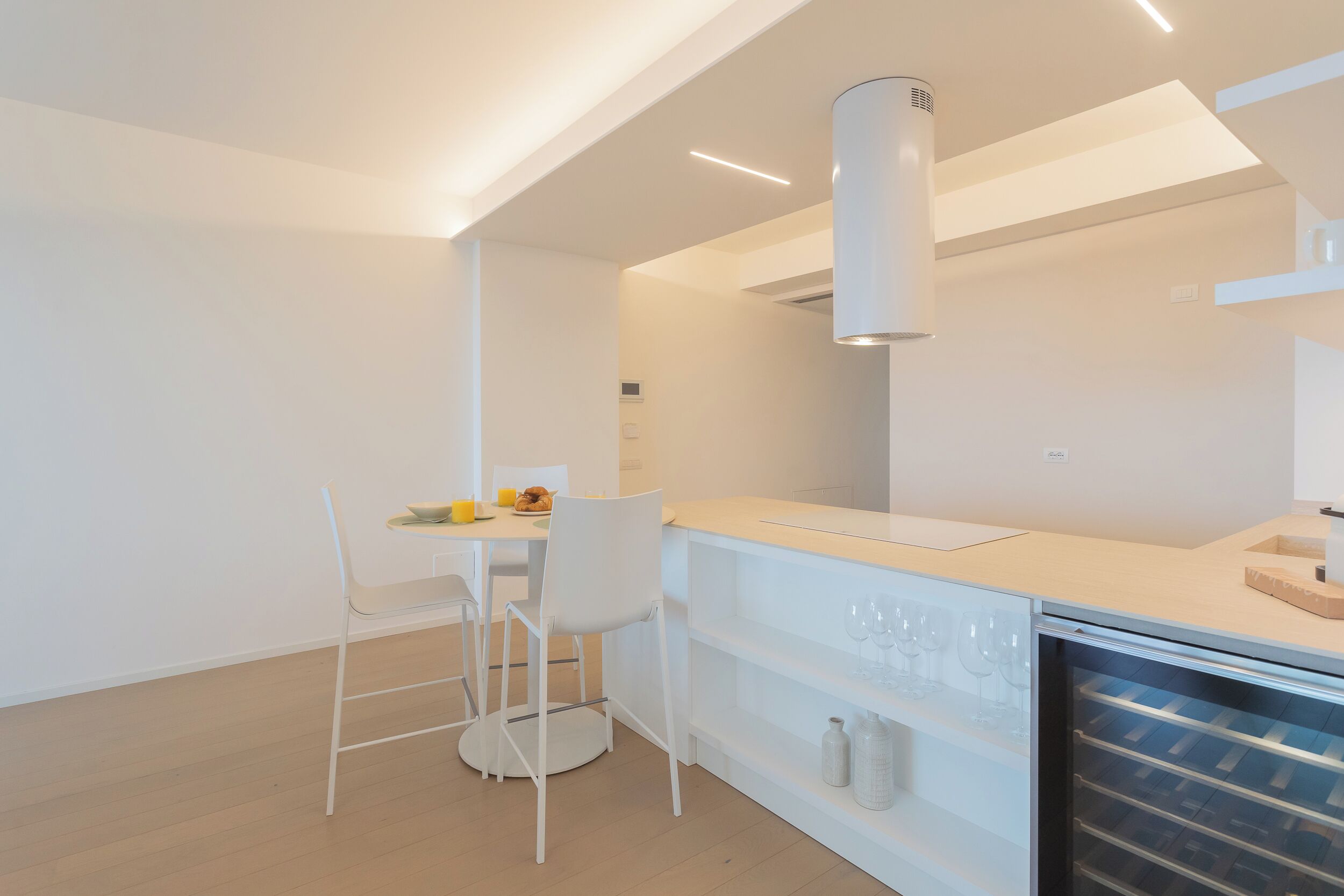 A modern kitchen with white cabinetry, a built-in wine cooler, and a dining area with a white table and chairs.