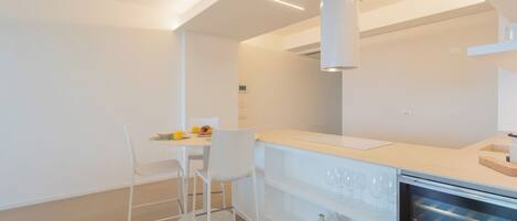 A modern kitchen with white cabinetry, a built-in wine cooler, and a dining area with a white table and chairs.