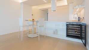 Una cocina moderna con armarios blancos, horno empotrado y una zona de comedor con dos sillas blancas.