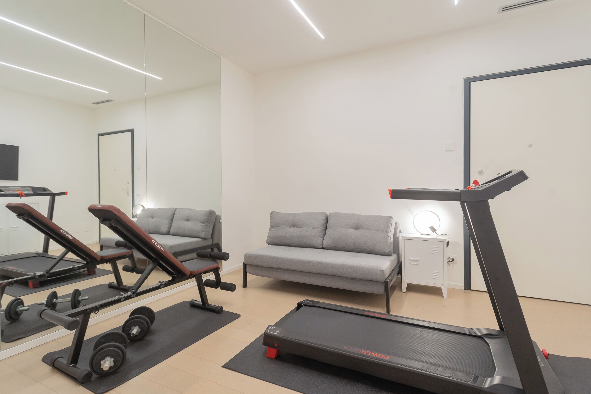 A home gym with a treadmill, bench press, and dumbbells.