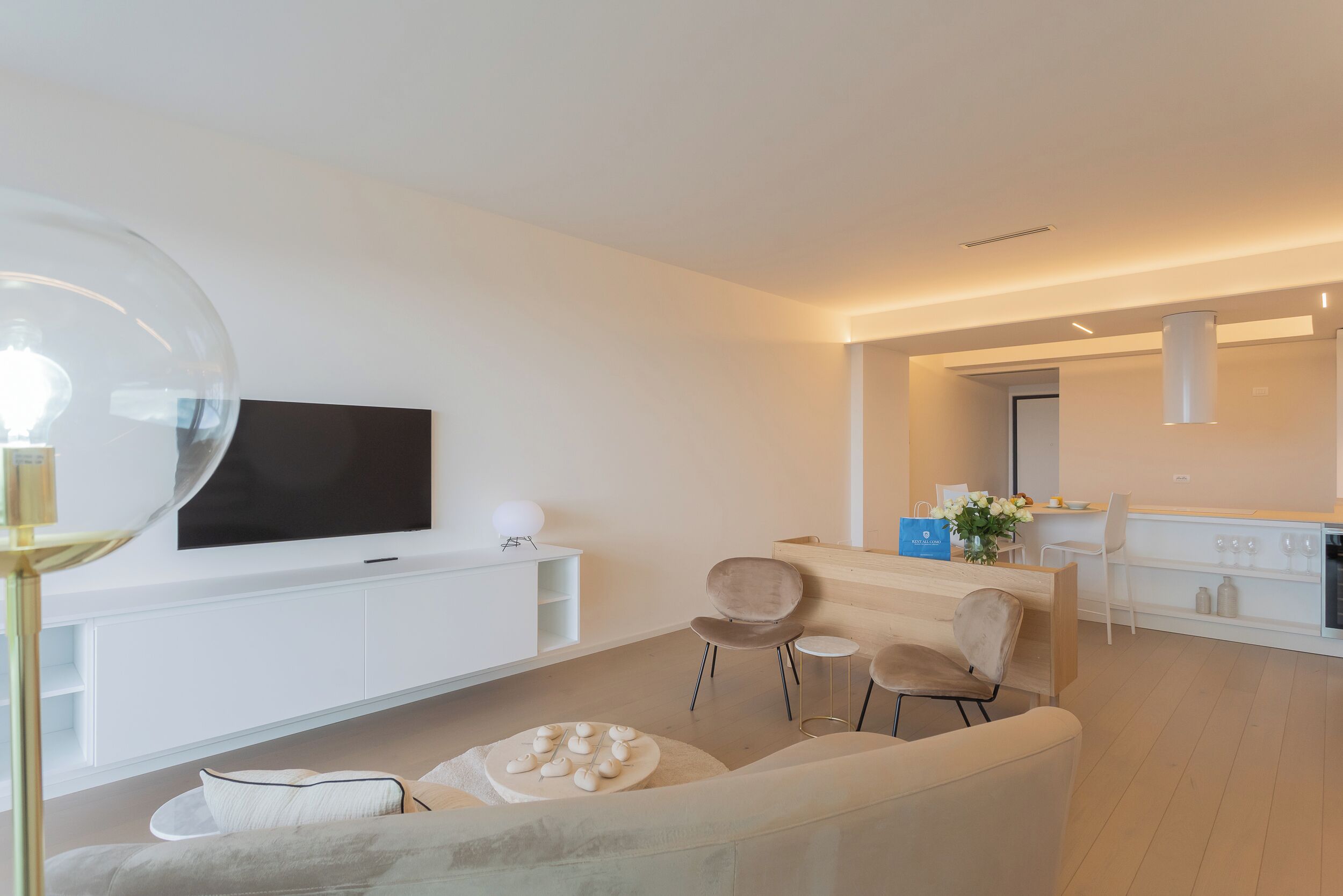 A modern living room with a flat-screen TV, a sofa, a coffee table, and a dining area with chairs and a small table.