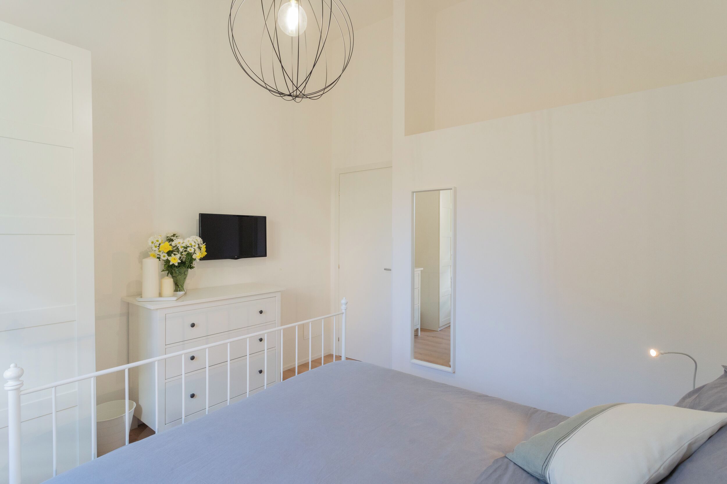 A bedroom with a bed, a dresser, a TV mounted on the wall, and a mirror.