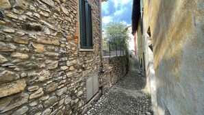 A narrow cobblestone alley between stone buildings with shutters, a metal gate, and a clear sky. - Mezzegra Apartments by Rent all Como (Tremezzina)