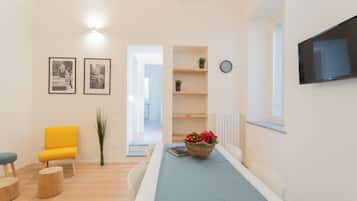 Una sala de estar moderna con una mesa de comedor, una silla amarilla, un mantel azul y un televisor de pantalla plana en la pared.