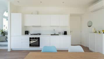 A modern kitchen with white cabinetry, a built-in oven, and a dining area with a wooden table and blue chairs.