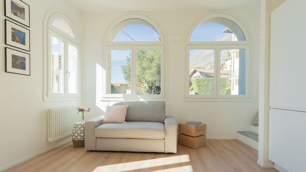 A spacious living room with a sofa, a radiator, and large arched windows offering a view of the outside. - Mezzegra Apartments by Rent all Como (Tremezzina)