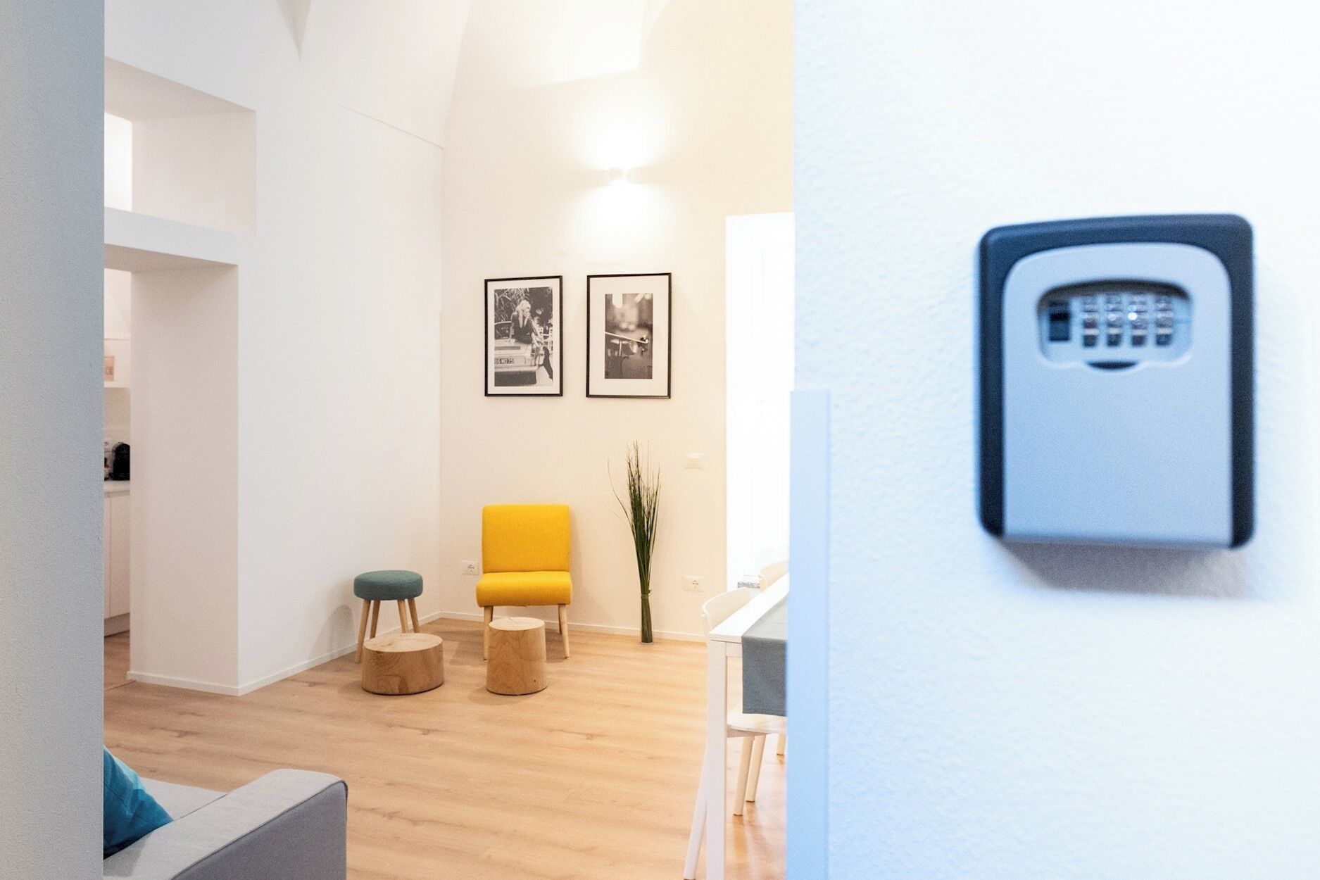 Una sala de estar moderna con una silla amarilla, taburetes de madera y cuadros en la pared.