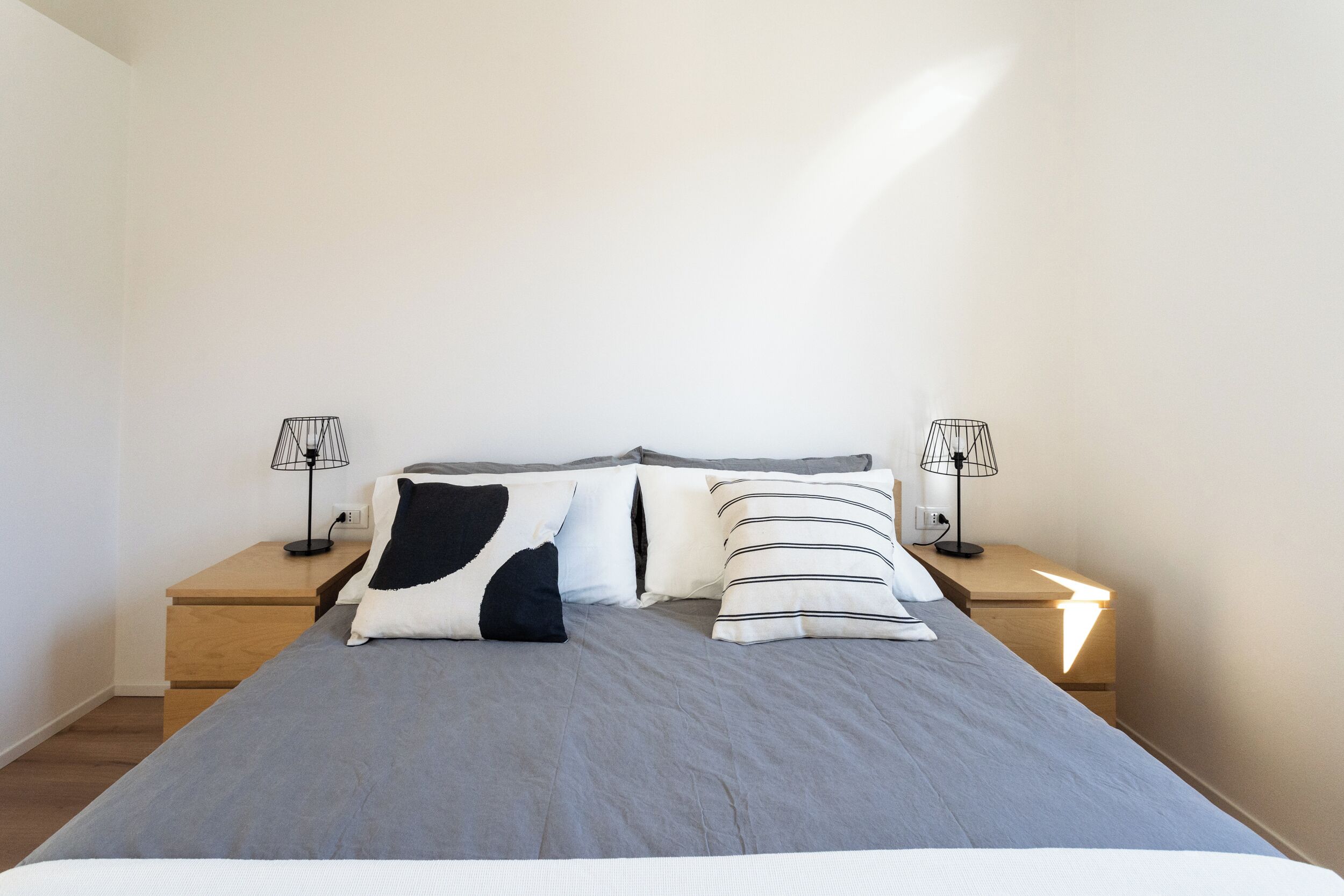 Un letto rifatto con riga grigia e due cuscini, affiancato da due comodini con lampade.