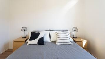 Un letto rifatto con riga grigia e due cuscini, affiancato da due comodini con lampade.