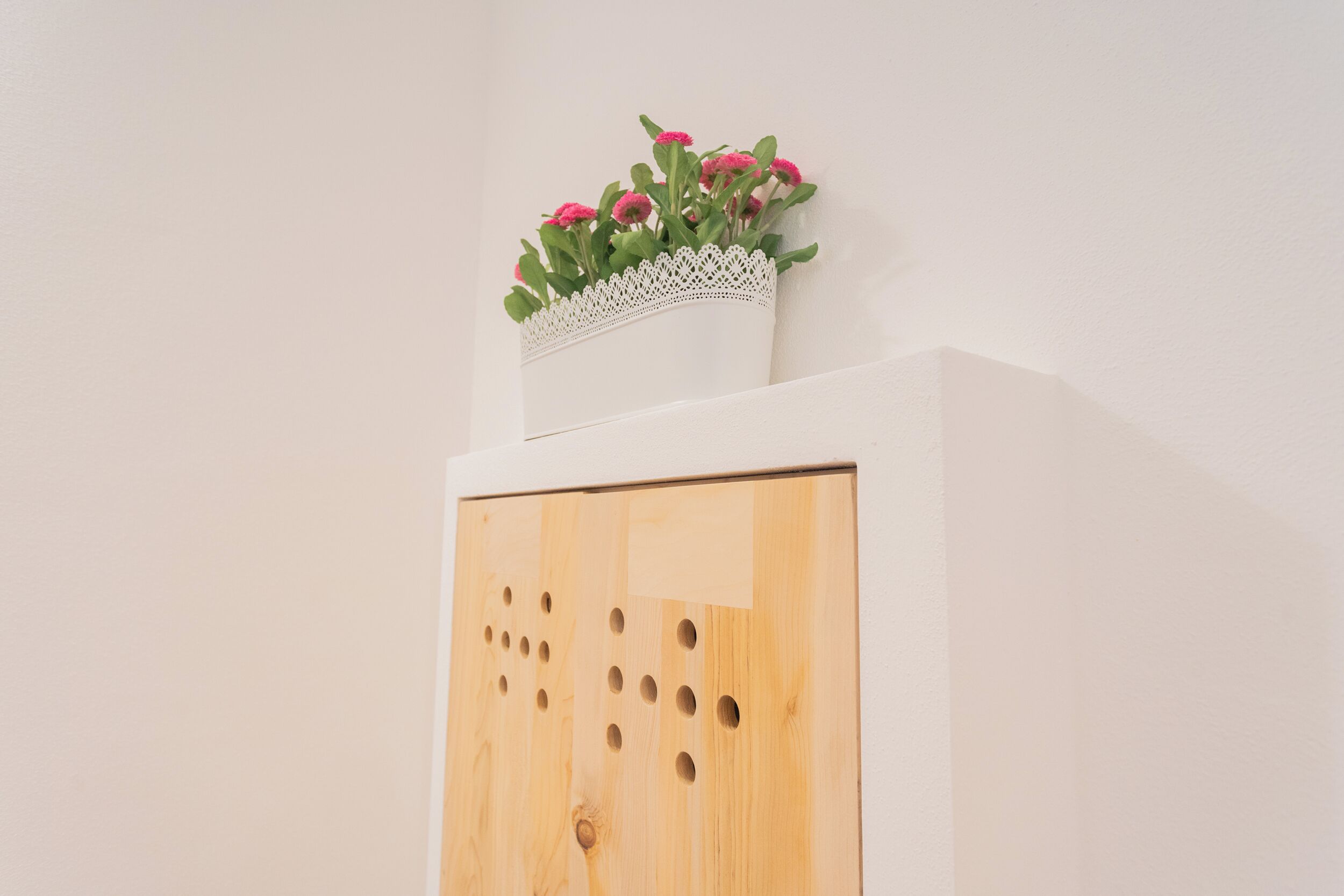 A wooden cabinet with a white vase containing pink flowers on top.