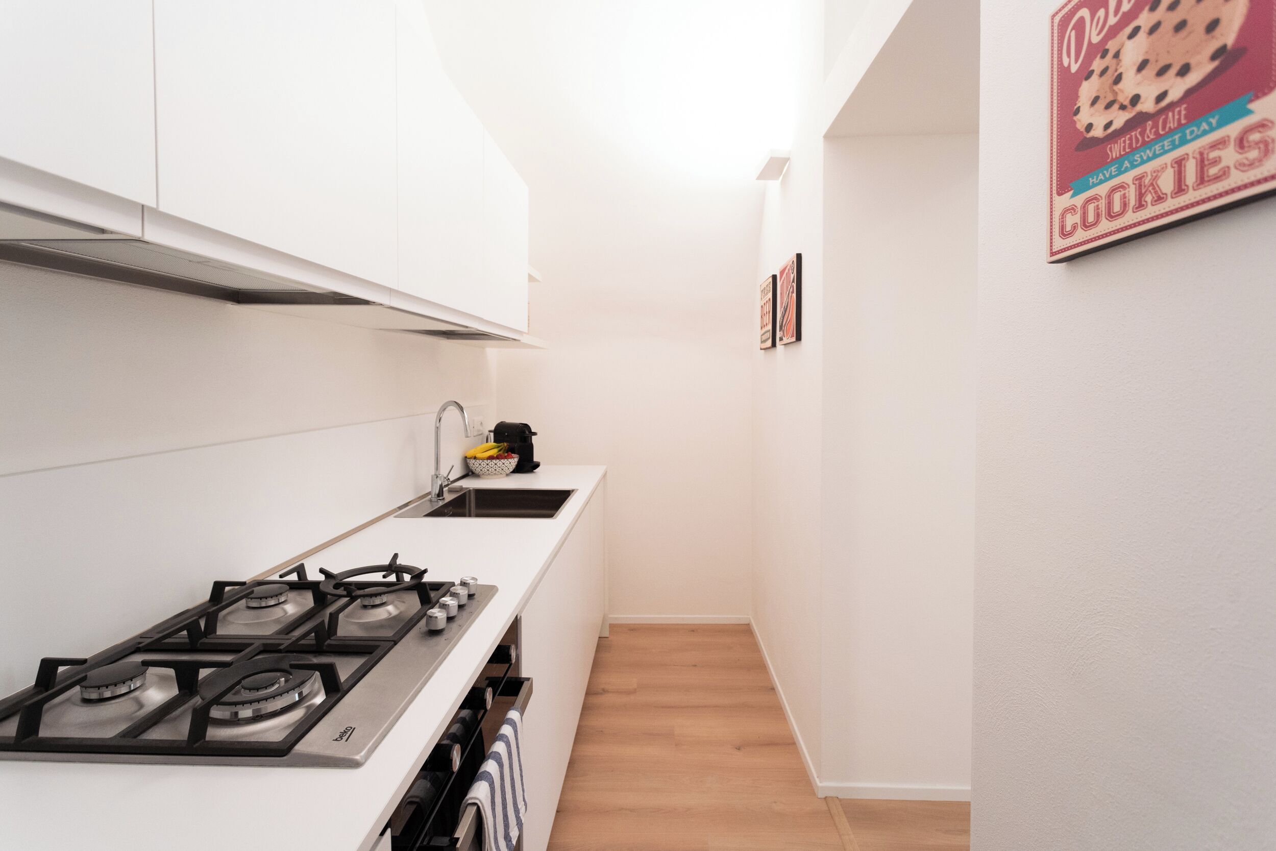 A narrow kitchen with white cabinets, a gas stove, and a coffee maker on the counter.