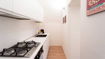 A narrow kitchen with white cabinets, a gas stove, and a coffee maker on the counter.