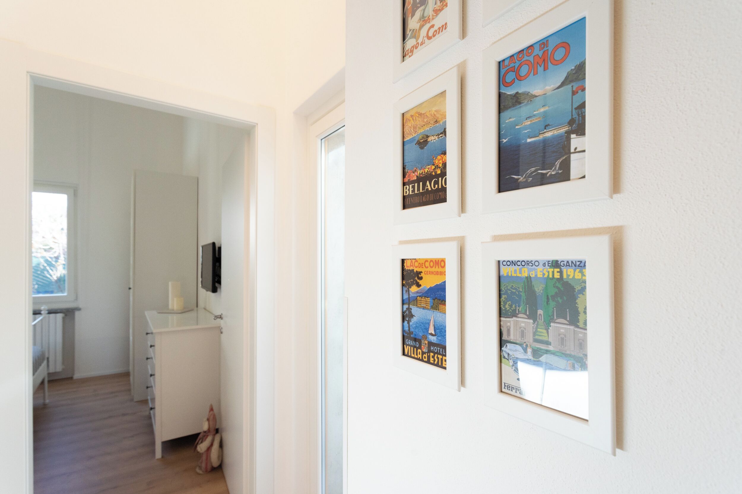 A hallway with a white wall, a framed poster of a coastal scene, and a white cabinet with drawers.