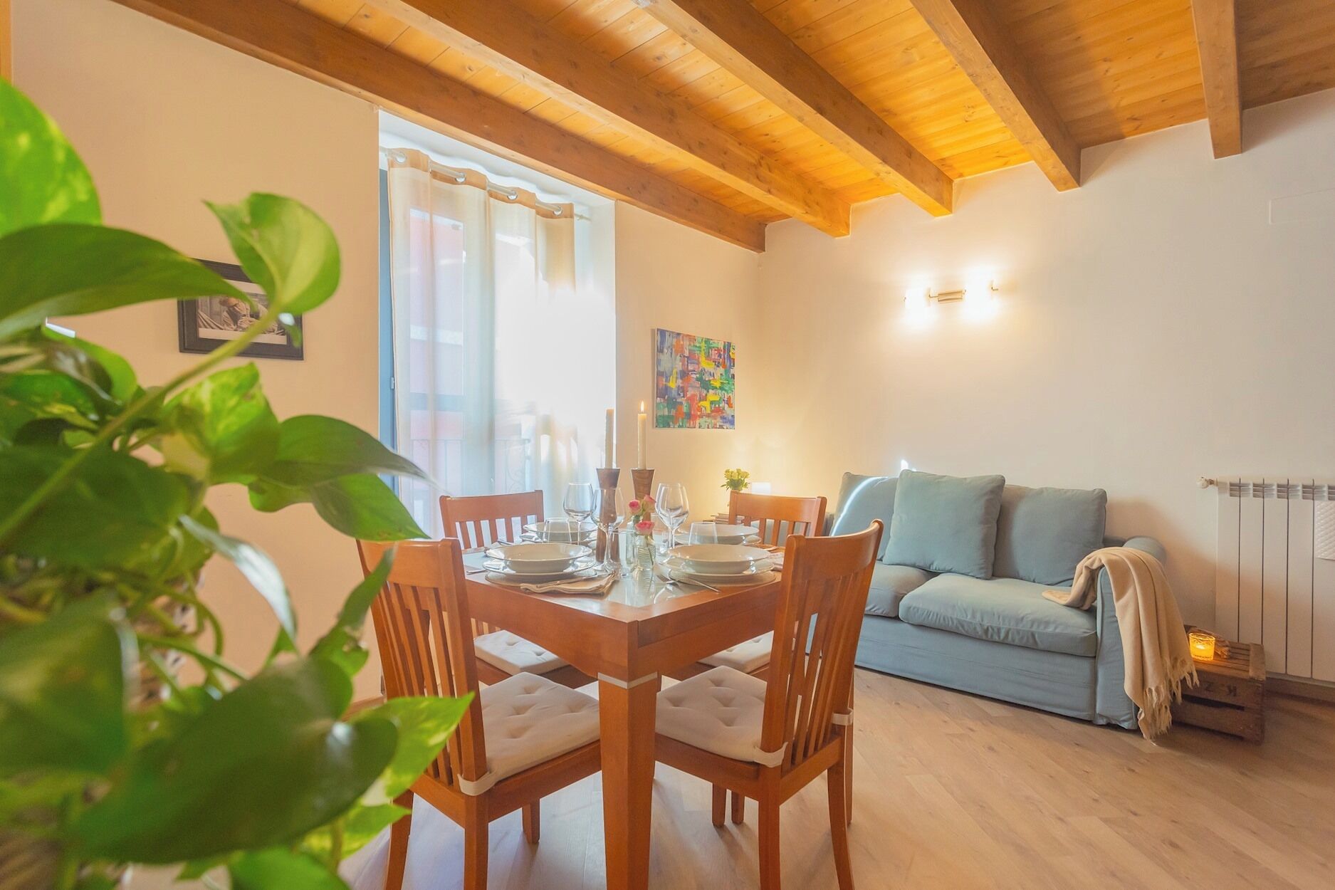 Un comedor con sillas de madera y una mesa preparada para cuatro personas, un sofá azul claro y un radiador.